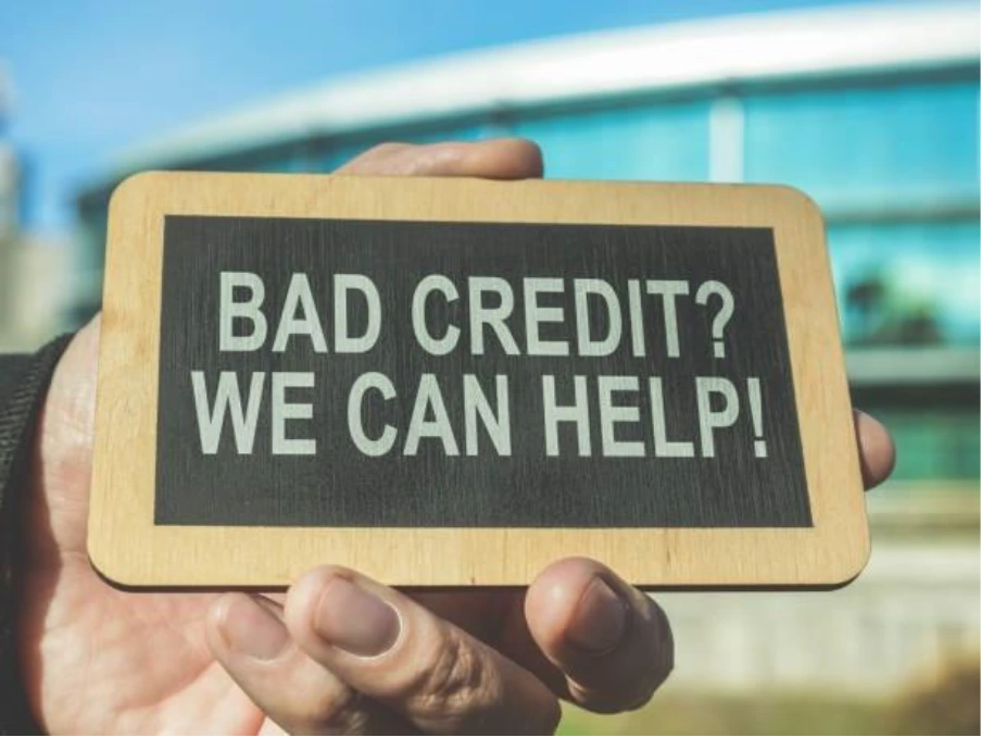 Hand holding sign reading “Bad Credit? We Can Help” outside residential property