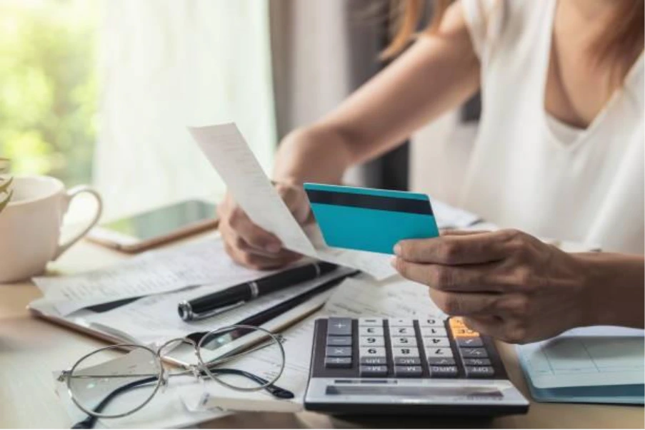 Person reviewing credit card statement with calculator and paperwork during mortgage assessment