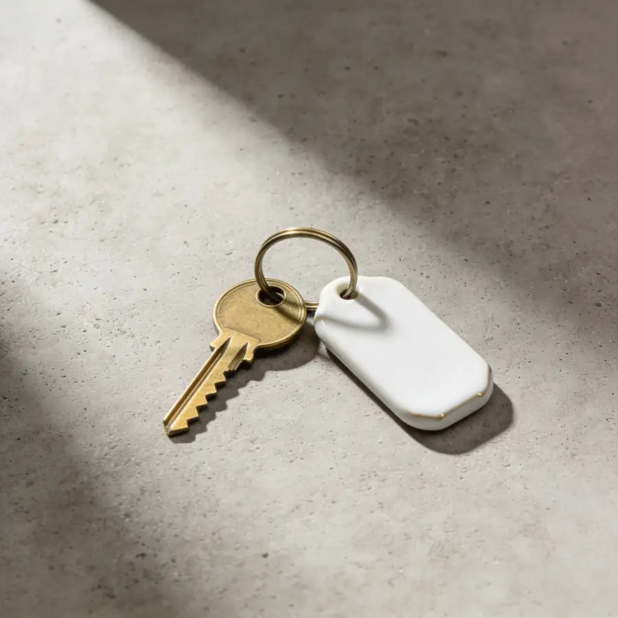 Modern brass door key with white ceramic tag on grey concrete surface representing first-time buyer mortgage completion